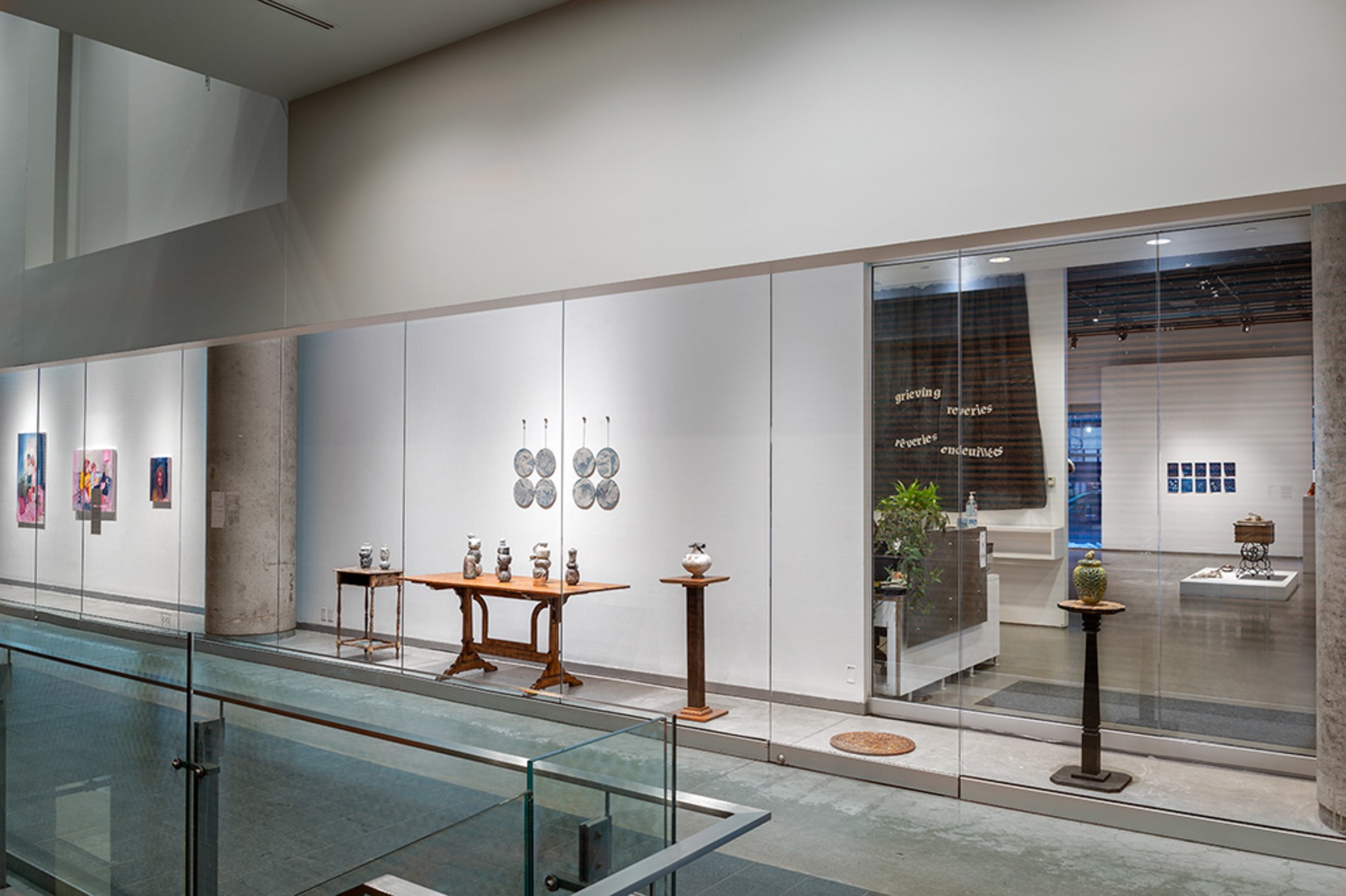 Vue de l'installation d'une vitrine dans un couloir ; l'installation se compose de divers meubles en bois foncé sur lesquels sont disposés des vases en céramique, ainsi que de deux séries d'assiettes bleues fixées au mur.