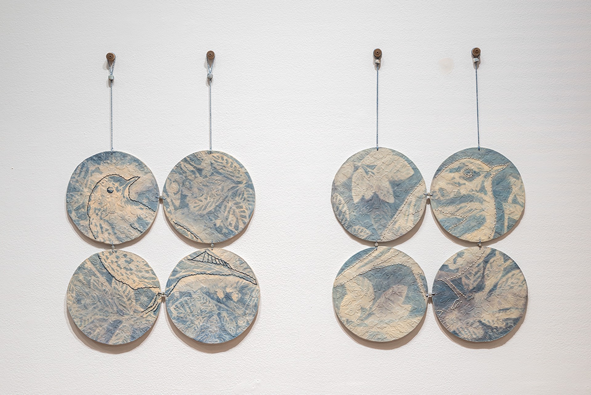 Deux séries de quatre assiettes rondes bleu pâle accrochées au mur, ornées de deux oiseaux et de quelques fleurs.