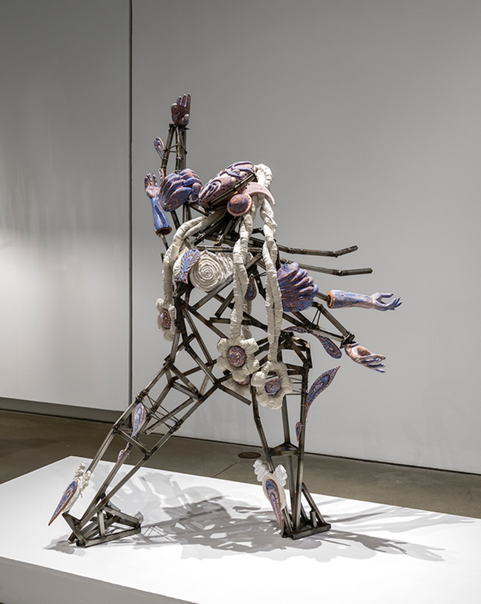Sculpture représentant une figure robotique composée de pièces métalliques et textiles, l'un de ses quatre bras levé vers le ciel. 