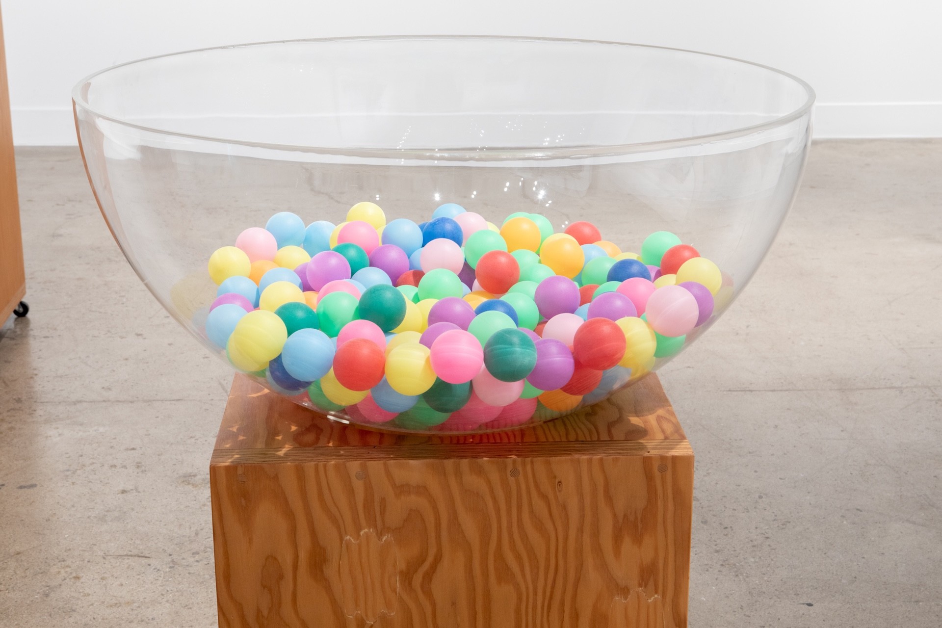 Gros plan sur un socle dans lequel est encastré, au centre, un bol transparent. Le bol est rempli de balles de ping-pong multicolores.