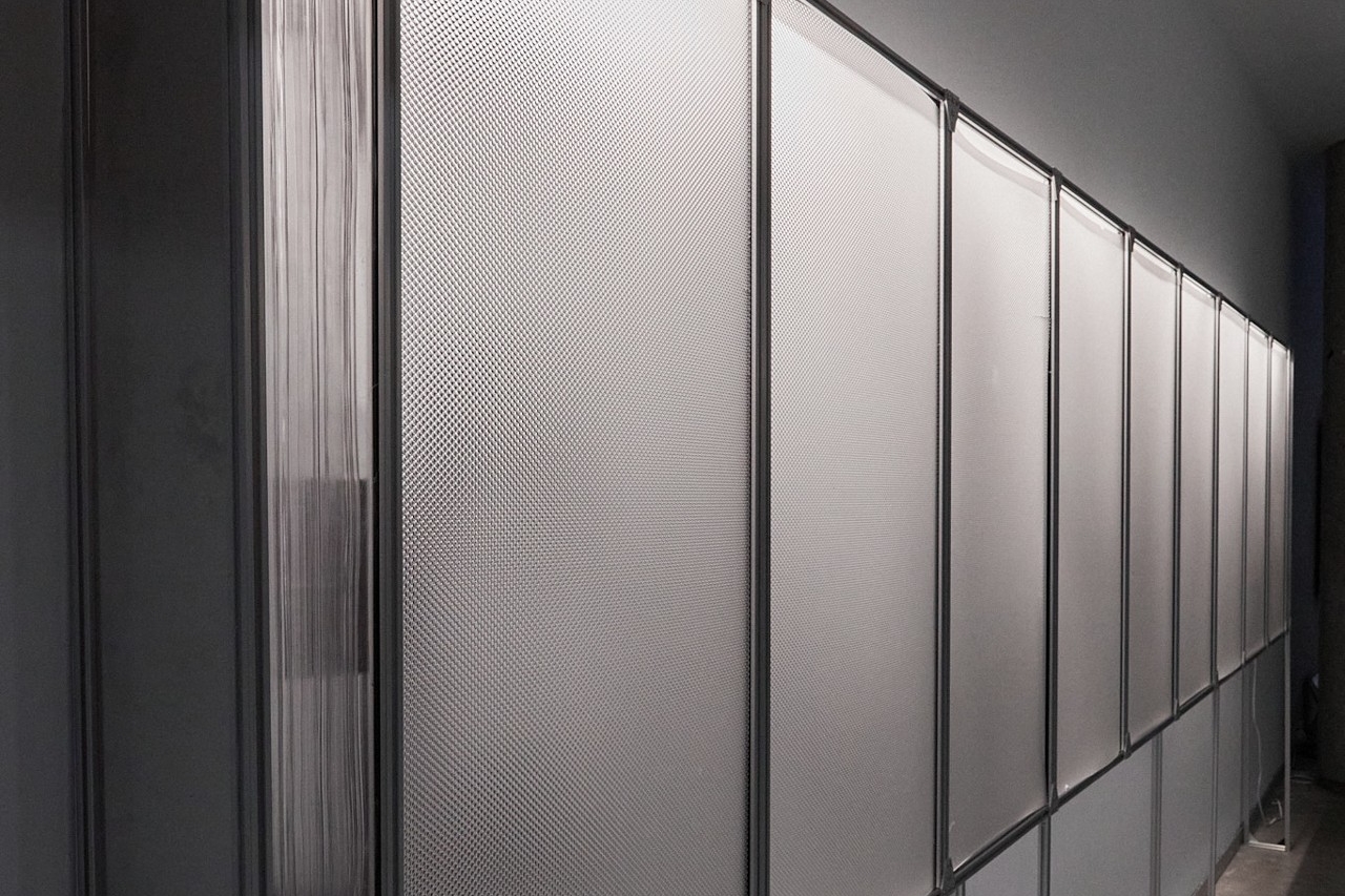 Vue détaillée prise sous un angle latéral gauche d'une structure métallique de 1,80 m de long, éclairée de l'intérieur par des néons. Sous cet angle, les panneaux frontaux rendent le texte illisible.