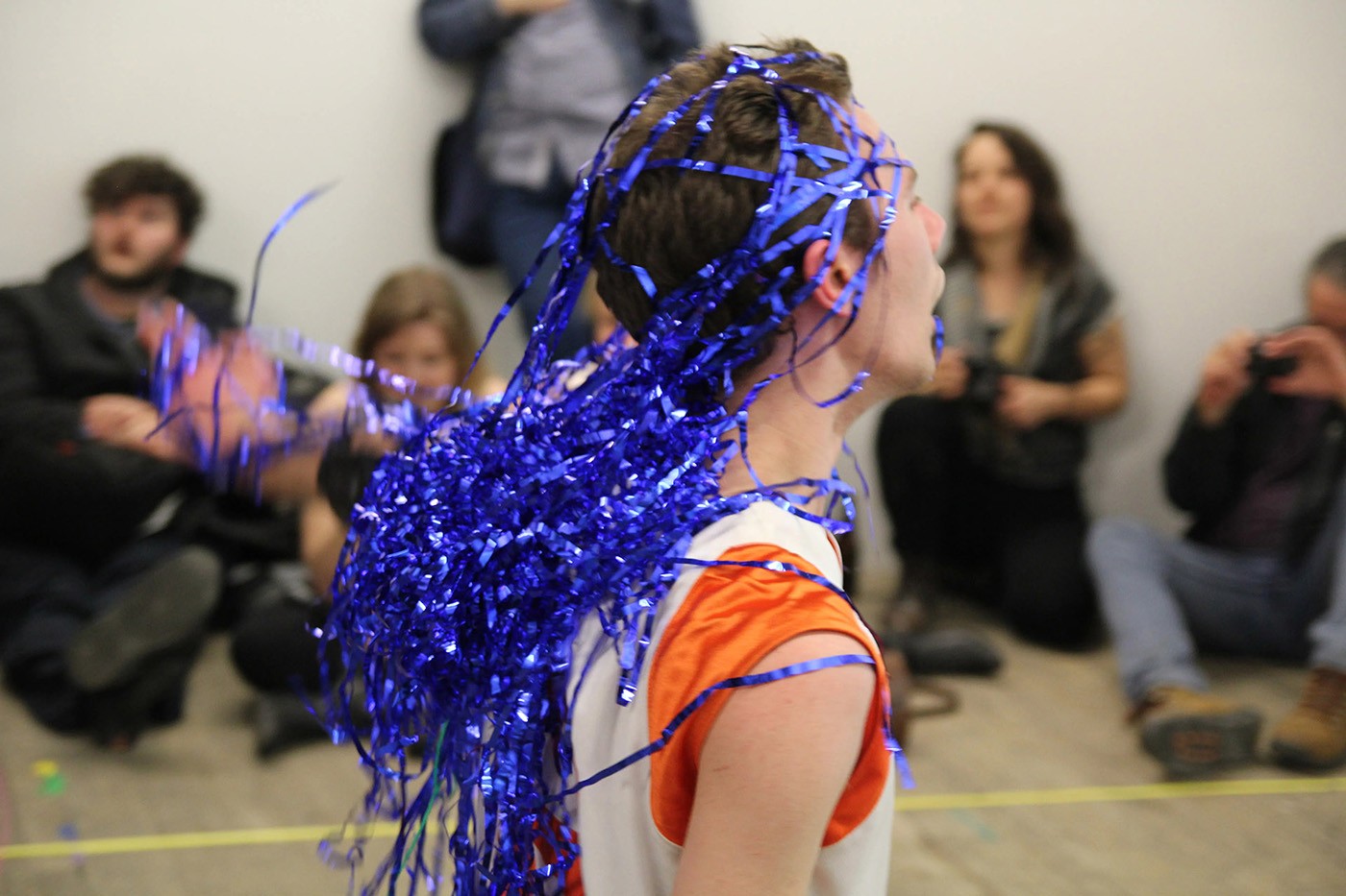 A performance artist running with a bleu tinsel curtain on his head. 