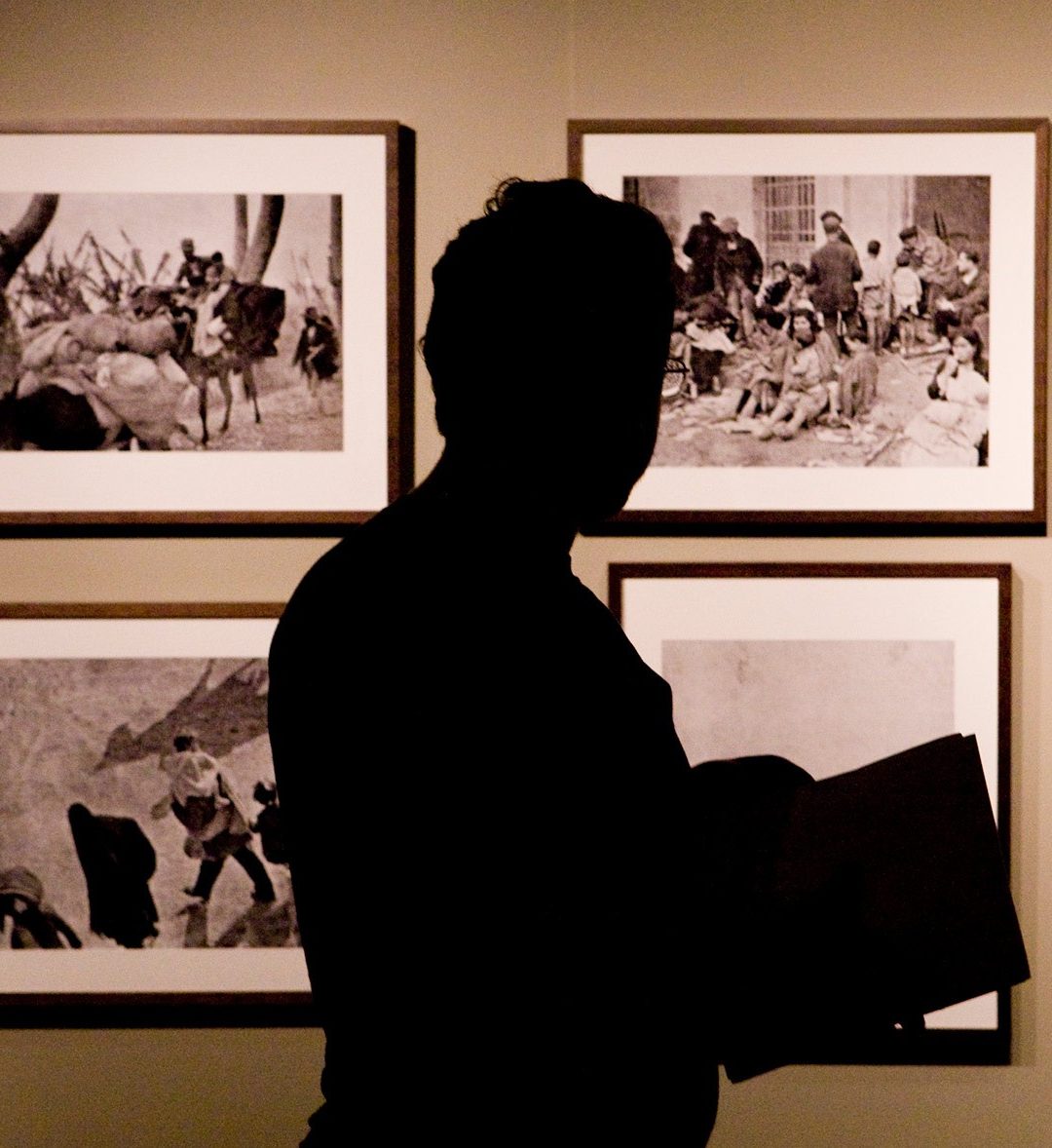 The silhouette of a person walking though a gallery exhibiting black and white photography and taking notes