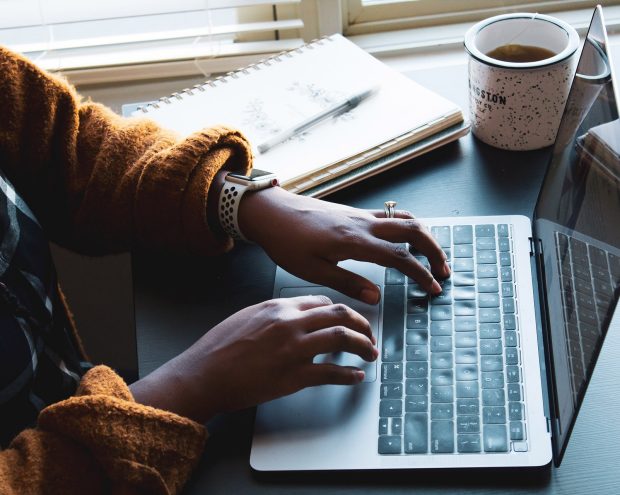 a person working on their laptop with a cup of tea and a notebook at their side