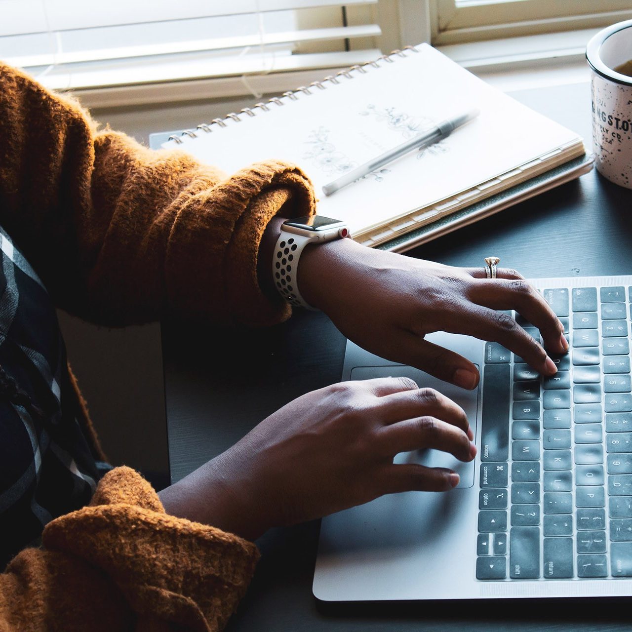 a person working on their laptop with a cup of tea and a notebook at their side