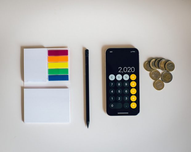 A flat lay of some post-it notes, a pencil, a calculator and some coins