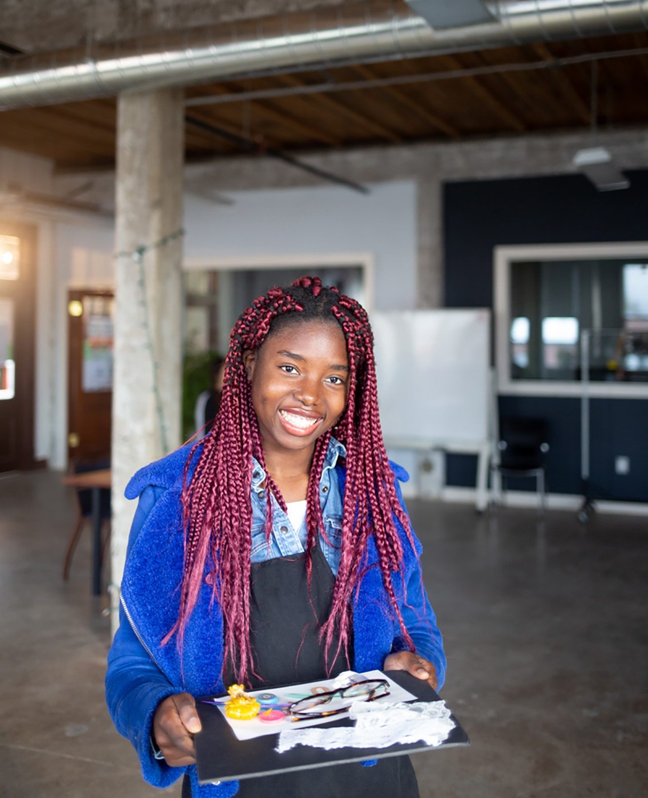 Female BIPOC student holding art supplies and smiling at the camera