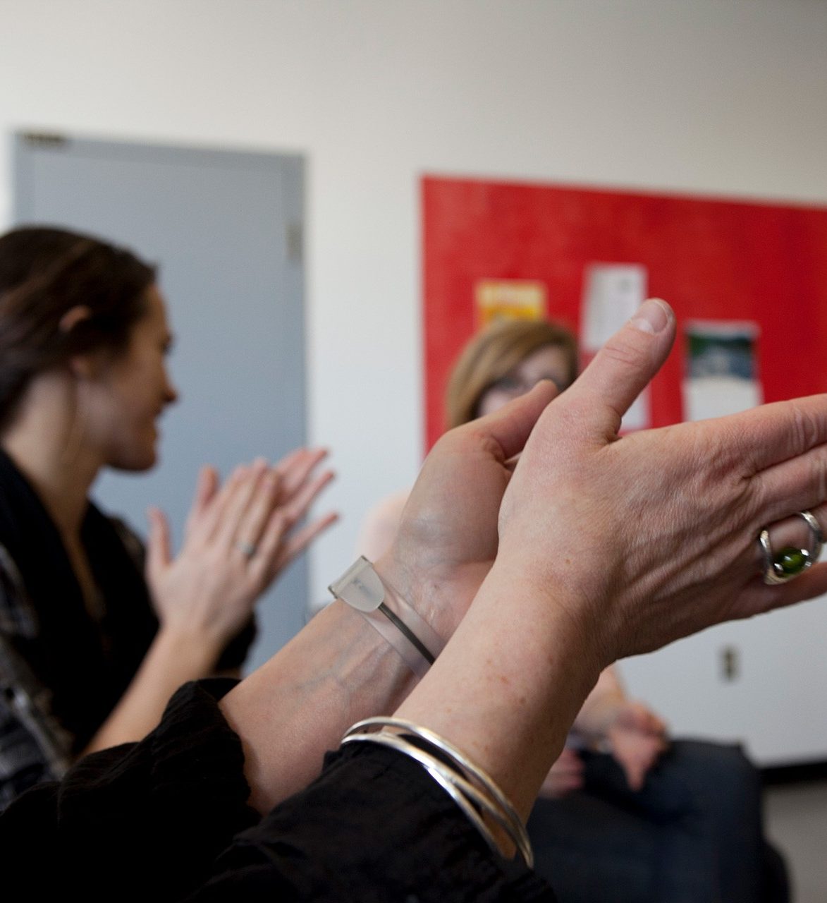 Close up of hands clapping; other participants clapping are in the background.