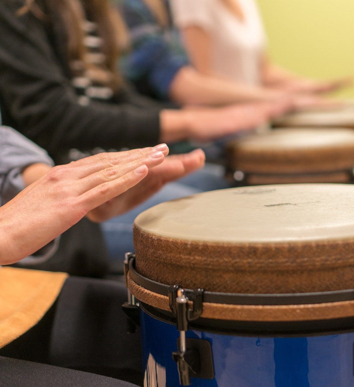 Close up of hands poised over a drum in the foreground.