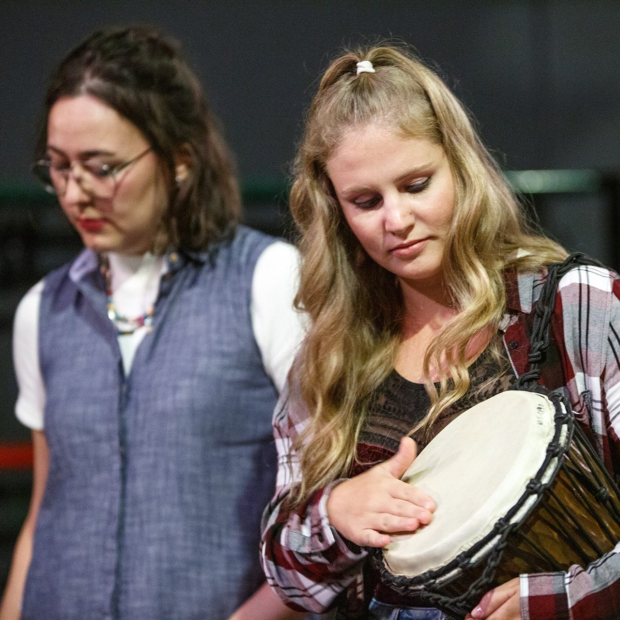 Creative Arts Therapies On a stage, a woman taps a hand drum.