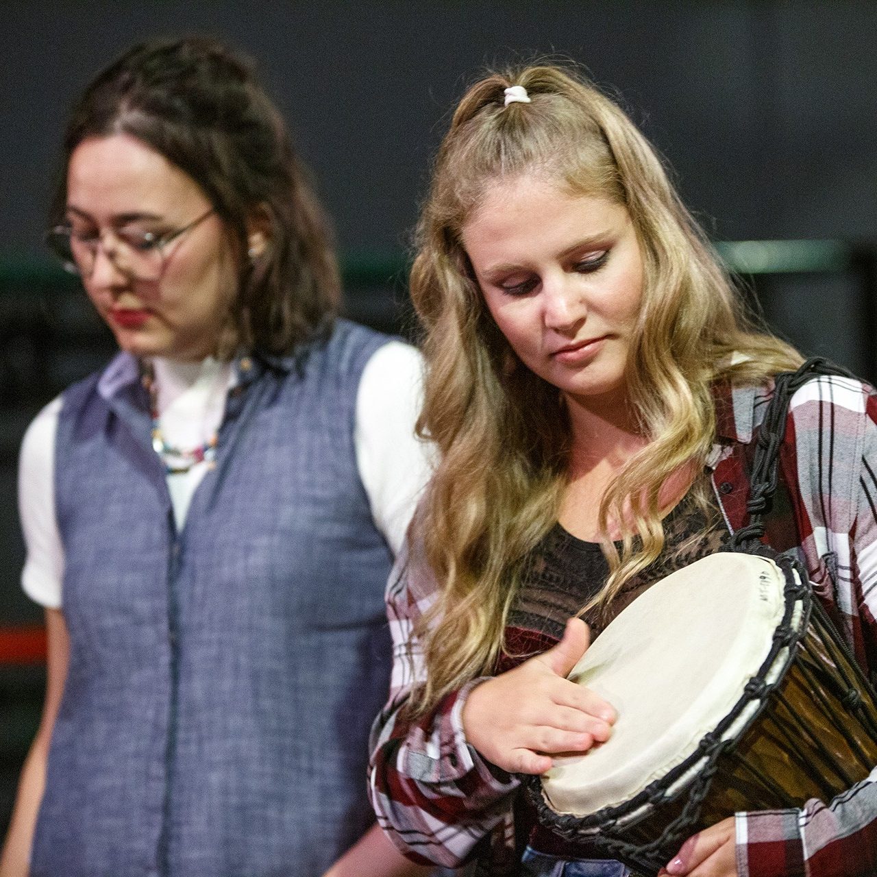 On a stage, a woman taps a hand drum.