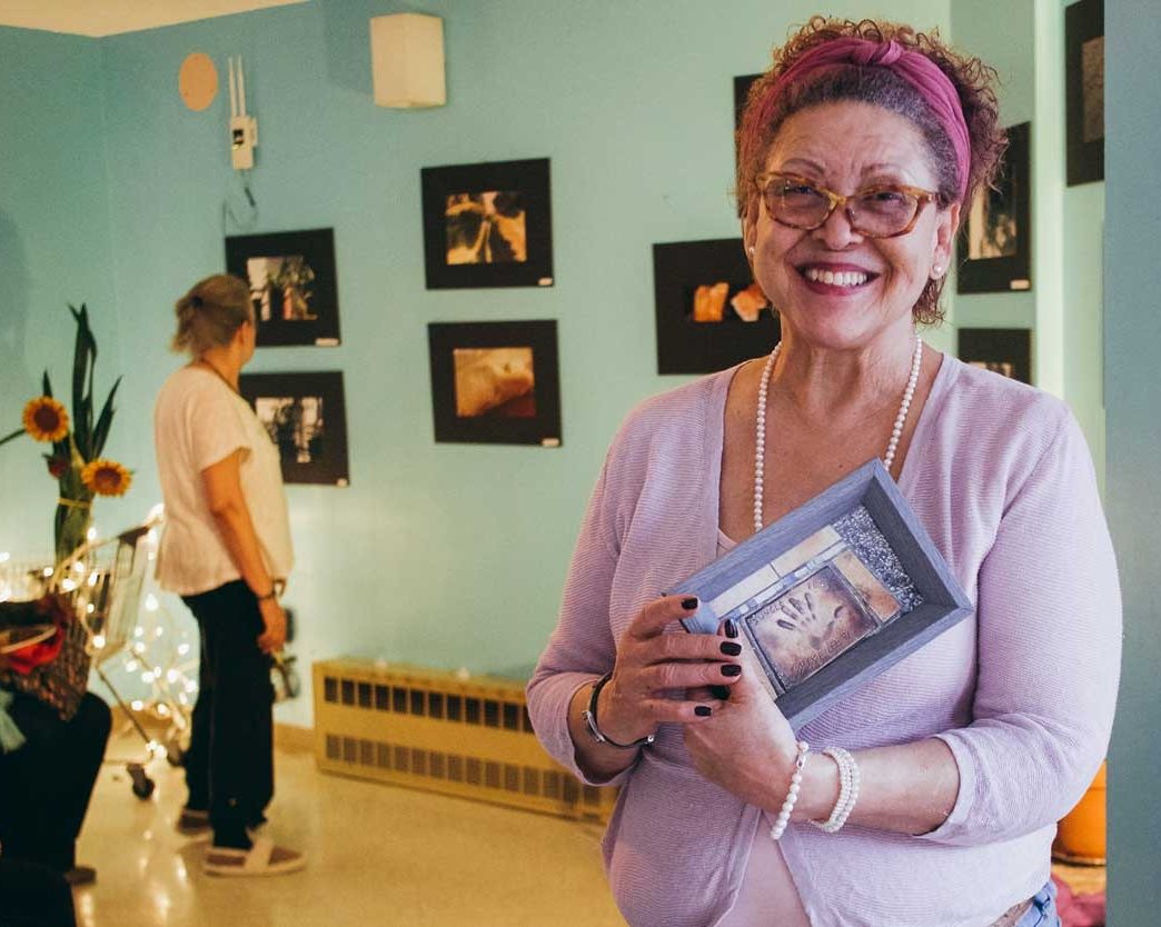 A smiling, active senior woman holds a picture frame artwork for the camera.