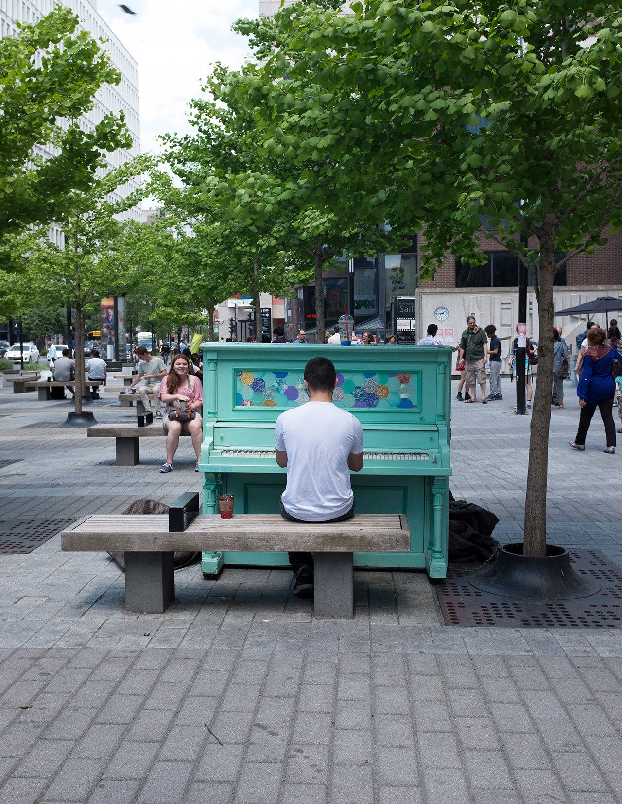 A young man sits at a turquoise-painted piano on a busy street in the Quartier Concordia in Montreal.