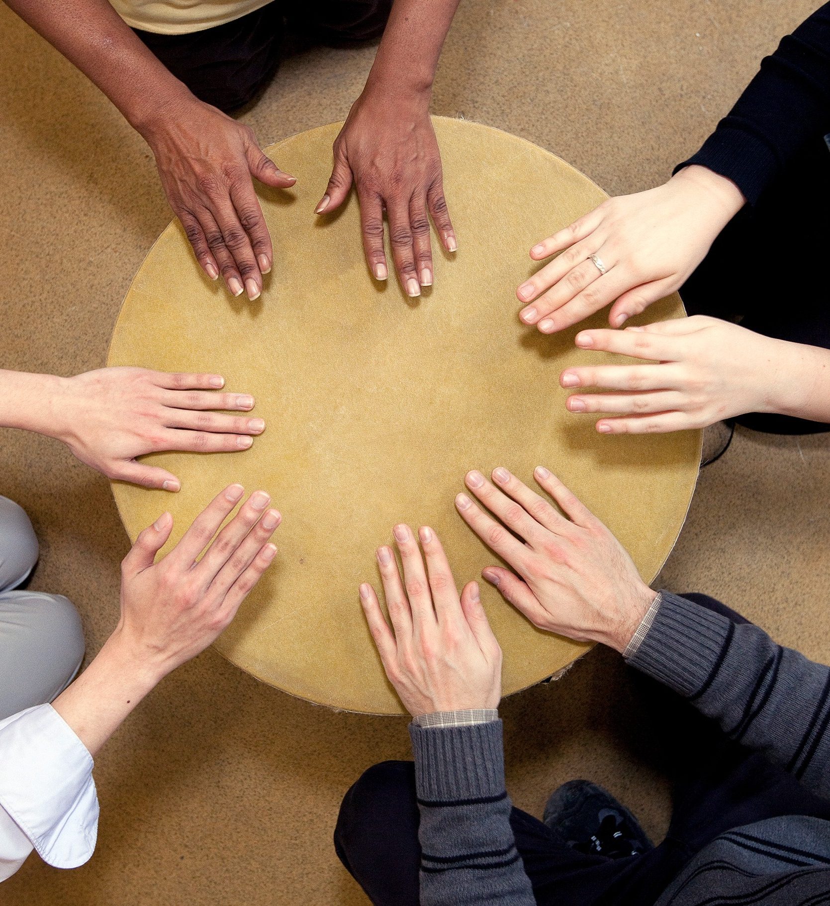 Four pairs of hands tap on a drum