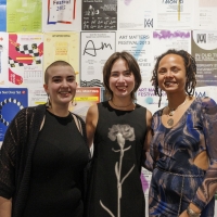 Three women smiling in front of a wall filled with posters advertising the Art Matters festival