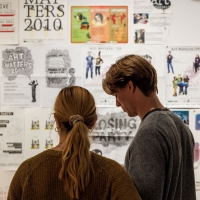 Three women smiling in front of a wall filled with posters advertising the Art Matters festival