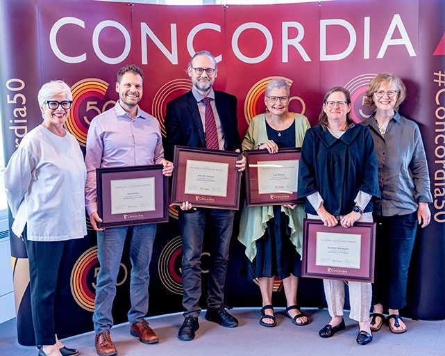 Group photo of people standing in front of Concordia billboard holding plaques