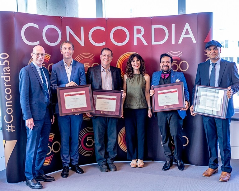 Group photo of people standing in front of Concordia billboard holding plaques