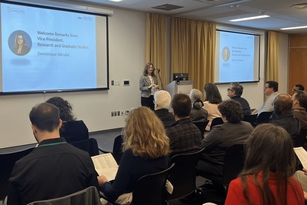 A person standing in front of an audience giving a speech during a slideshow presentation
