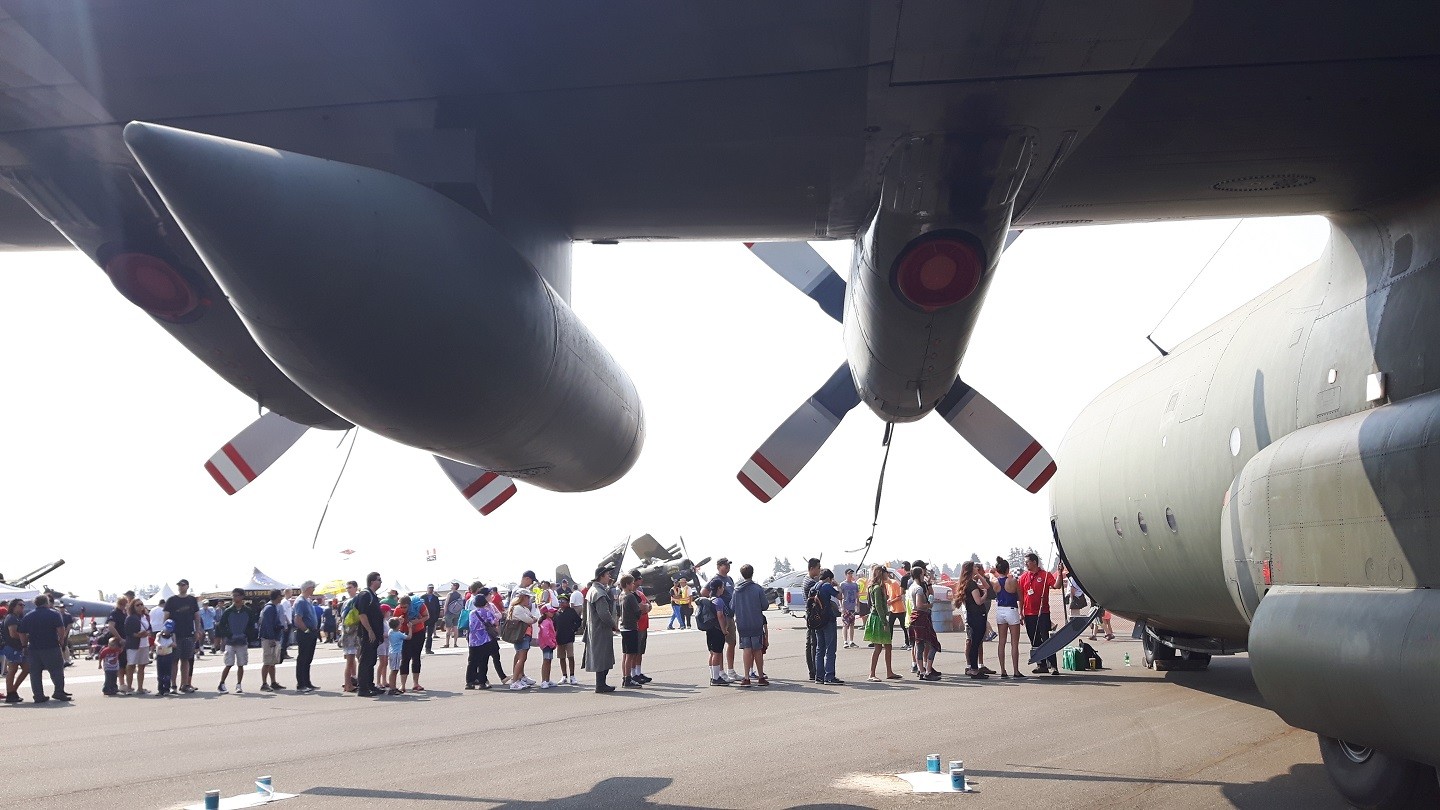 Approximately two-dozen people wait in line to visit the cockpit of a large military aircraft.