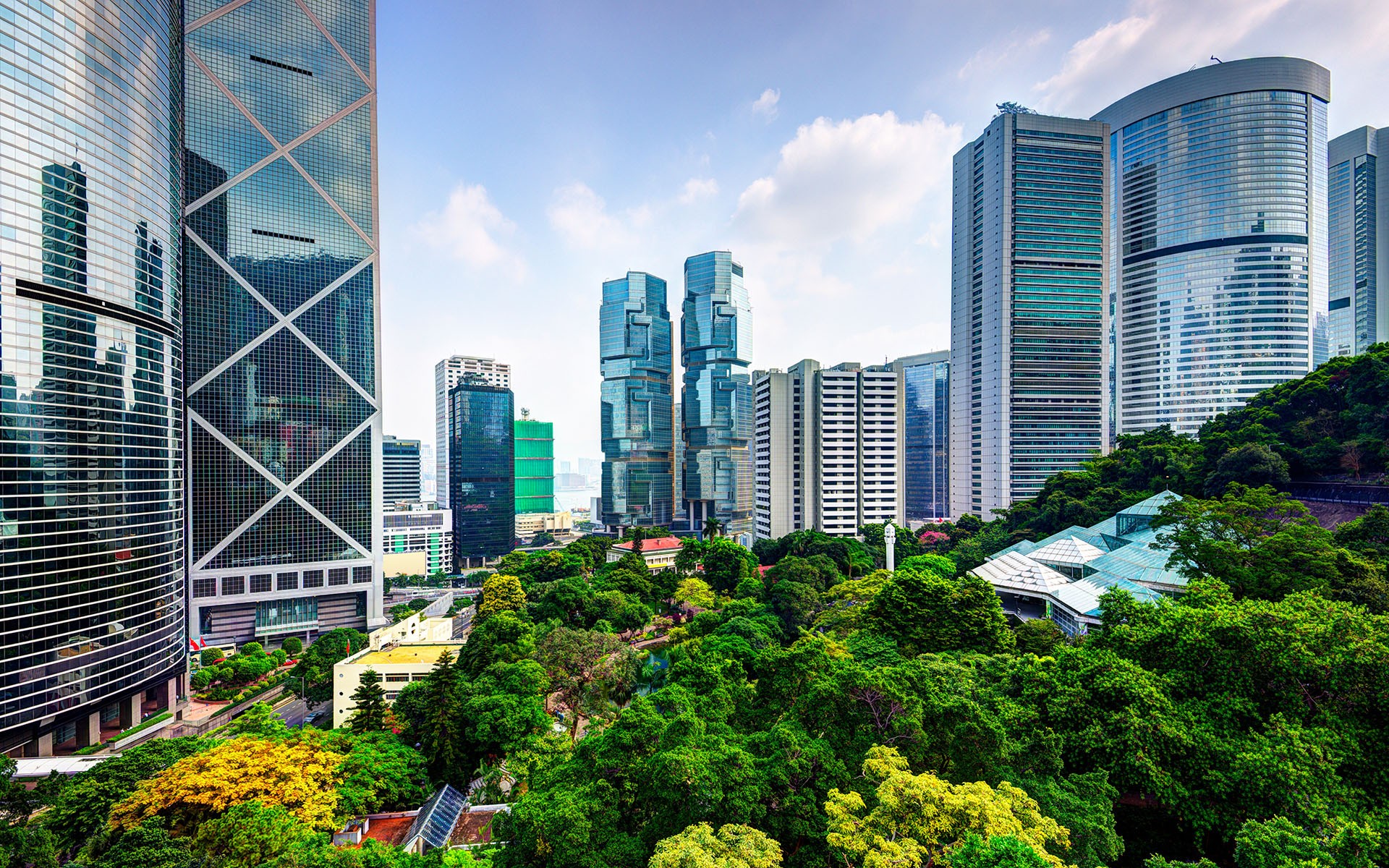 Photo of Hong Kong Park, which is a large urban green space with many trees and flower planting beds, located right next to several tall office buildings.
