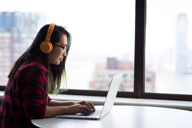 Person wearing orange headphones, working on a laptop