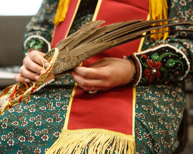 the hands of a person in traditional Indigenous clothing holding an object with feathers