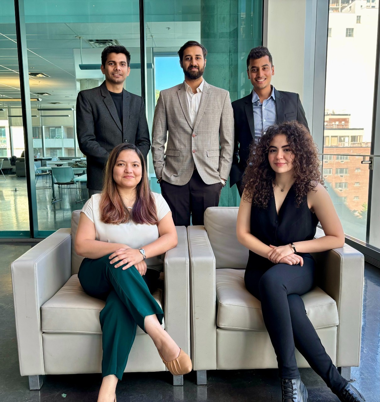 The 7 member of the team pose in the john Molson Building: 5 men stand behind 2 woman who are sitting in chairs