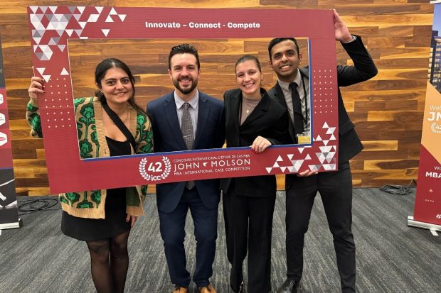 Four graduate students hold a cardboard frame with the JMSB MBA ICC logo