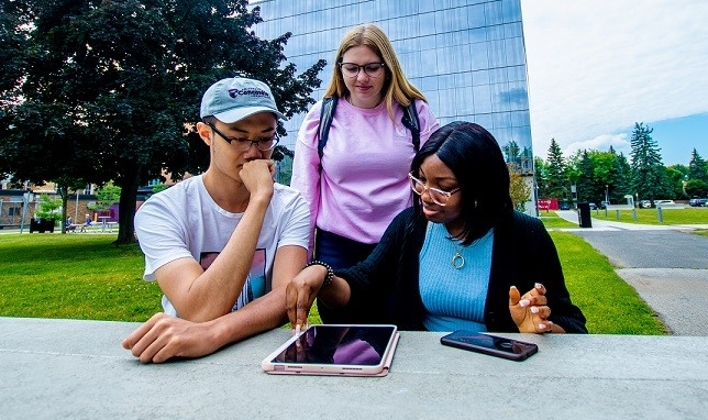 Three students are working together using a tablet at a table outside