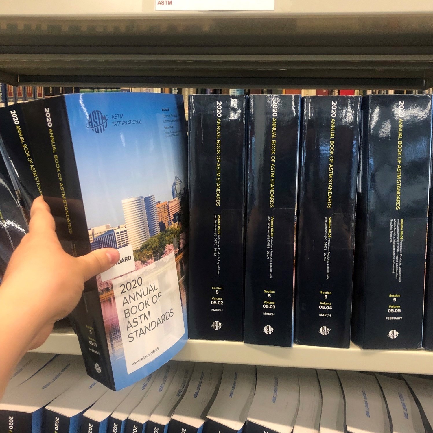 A hand retrieving a standard from a book shelf in the library