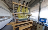 Loom machine stands in the middle of a cement room next to a computer and windows