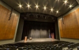 A theatre stage with black curtains and bright lights above it