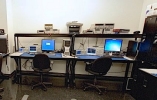 Two computers on a desk with shelves filled of computer parts