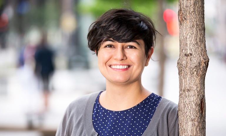 Young, smiling woman with short, dark hair and a blue top and grey cardigan.