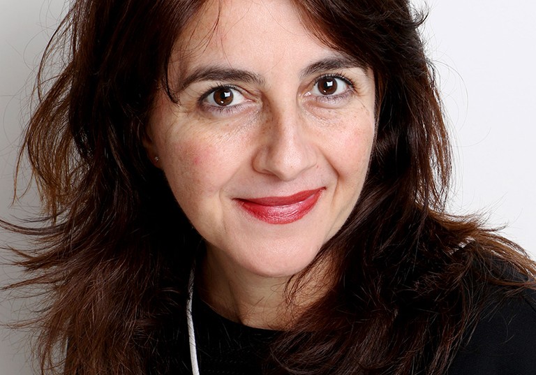 A smiling woman with dark, long hair and red lipstick.