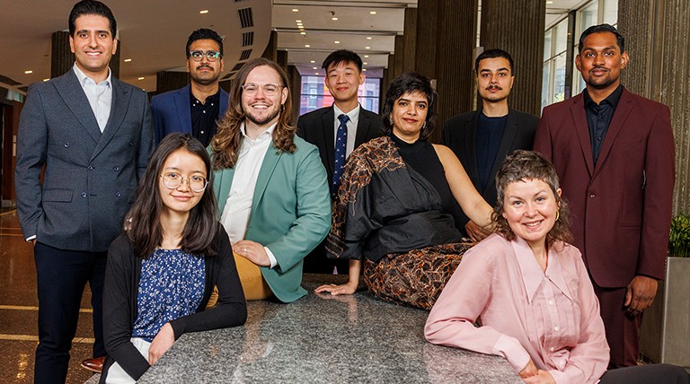 A diverse group of men and women seated and standing around a long table and smiling for the camera.