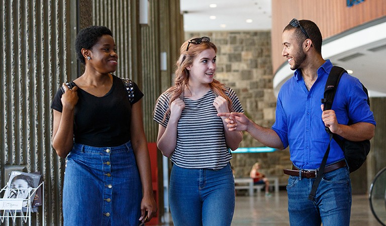 Two young women and a man speaking together and walking in an interior.