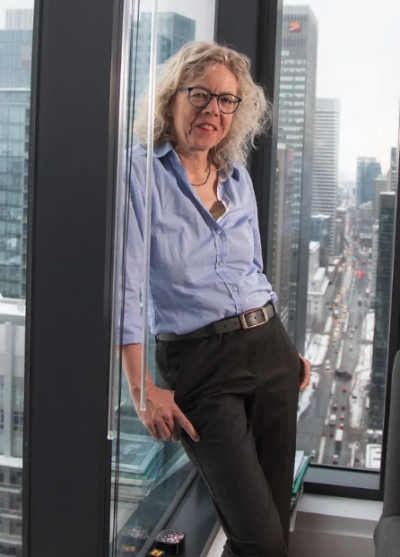 A woman with glasses smiles while standing in front of a city scape in an office building.