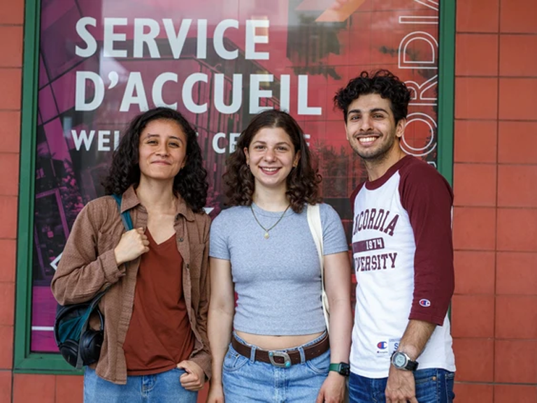 Three smiling students stand next to each other outside in summer attire. They smile as they face the camera. 