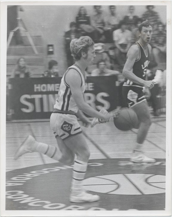 Men's basketball with player dribbling at middle court with opposing team looking towards