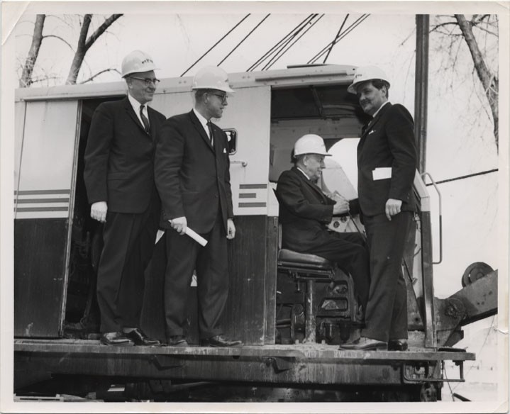 Group of construction workers in suits standing on an excavator