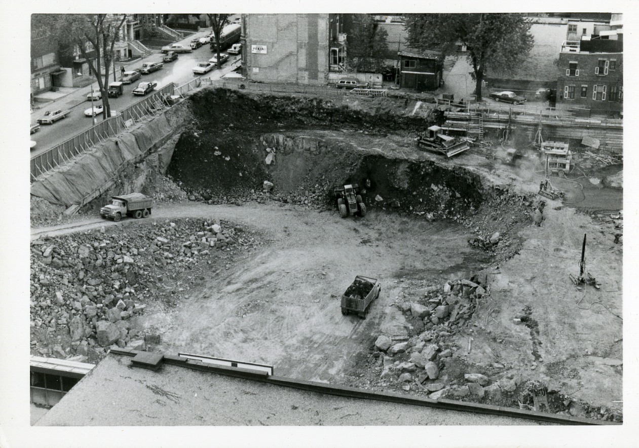 View of excavated dirt with trucks driving in and out of the site