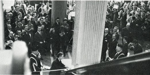 Group of people in suits watching the inauguration ceremony at the Hall Building