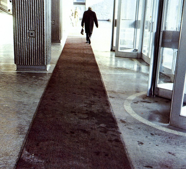 A person walking along a burgundy rug near the entranceway of the Hall Building
