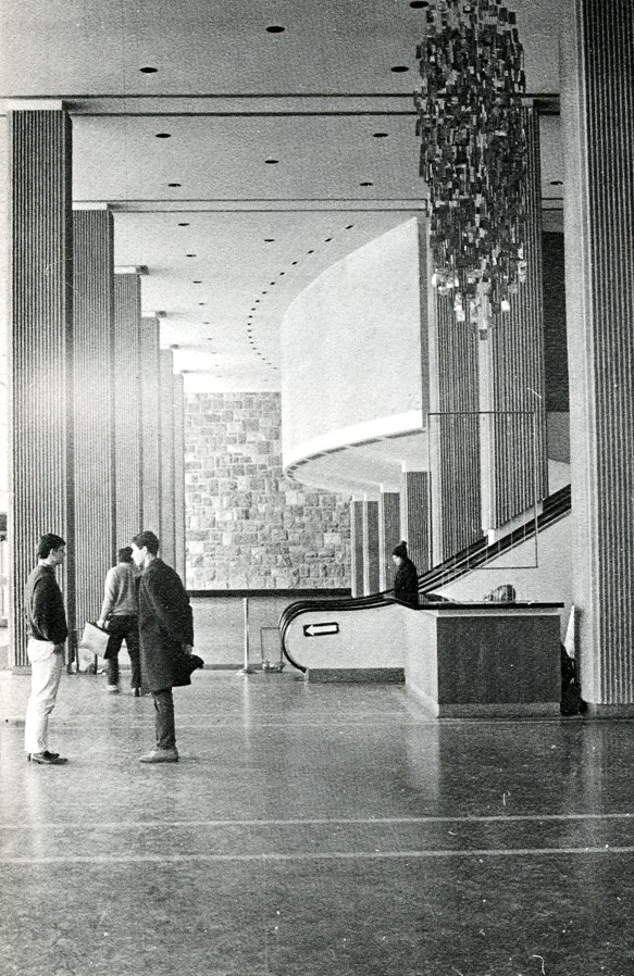People standing around talking in front of an escalator in the Hall Building lobby