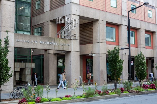 Street view of the J.W. McConnell Building entrance, featuring glass and stone facade, pedestrians and neatly arranged trees and flowers along the sidewalk.