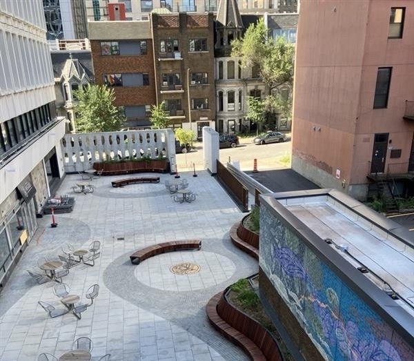 View of the renovated Henry F. Hall Building terrace from above, showing curved wooden benches, outdoor tables and chairs, landscaped planters, new brickwork and a central circular design.