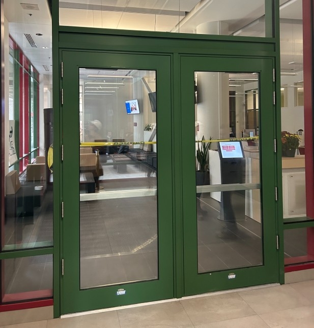 Interior view of the J.W. McConnell (LB) Building vestibule showing newly installed green-framed glass doors, with the lobby and seating area visible through the doorway.