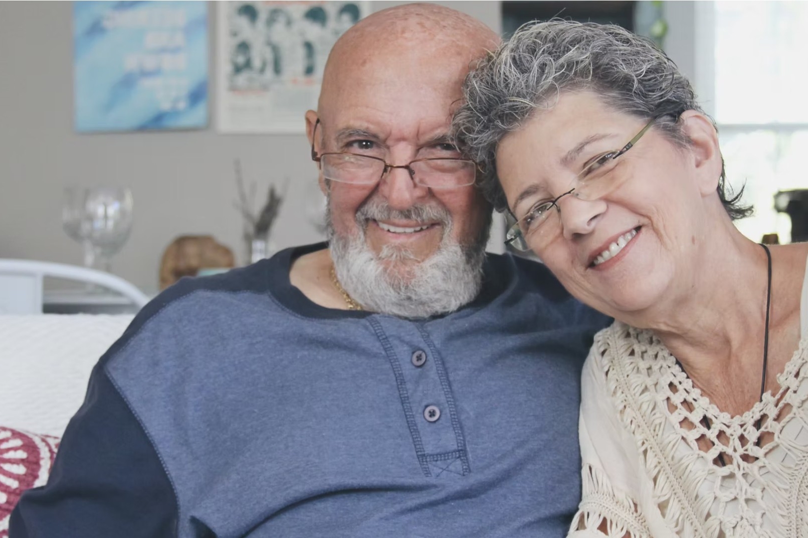 An older man and woman sit on a couch close to each other smiling